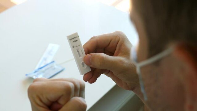Man check result of covid-19 rapid antigen test kit he did self at home, negative, recovered, man is happy. Adult male hold fast coronavirus atk with 1 stripe, not infected, takes off his face mask.