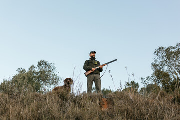 Hunter holding his gun standing smiling looking away in nature