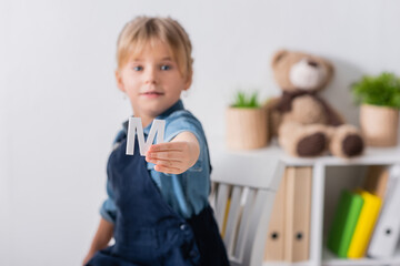 Blurred child holding letter and looking at camera in classroom.