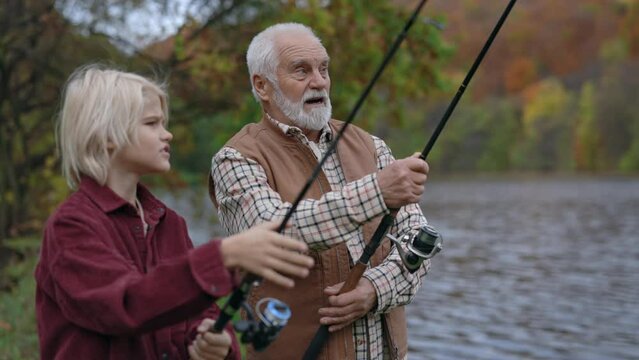 Caucasian boy using spinning rod for fishing with grandpa