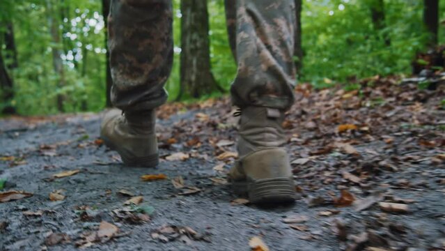 Close up soldier male legs in army boots walk falls to the ground wounded in camouflage uniform. In forest. Training. Imitation of hostilities