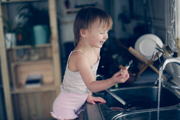 Toddler child washes his hands and fork in the sink in the kitchen, lifestyle in a real interior