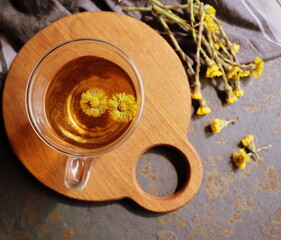 A cup of healing herbal tea for a stronger immune system with spring coltsfoot flower on background with medicinal plants Tussilago farfara and nettle. Top view. Flat lay