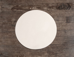 Round empty paper note in center of old weathered rustic wooden table. Top view. Mock up.