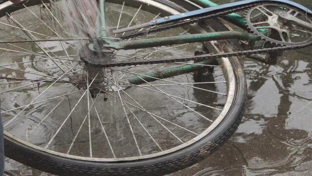 The wheel of an old dirty bicycle being washed with a jet of water.