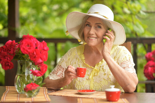 Beautiful smiling senior woman drinking coffee and talking on smartphone