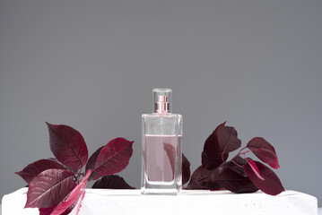 Frasco de perfume decorado con hojas de color  granate sobre fondo gris