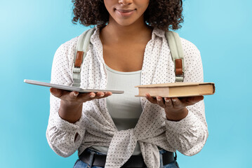 Cropped view of young black female student holding book and tablet pc, comparing offline studies...