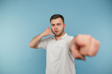 Naklejka premium Man with the bristles shows his fingers the gesture of the call and points his finger at the camera on a blue background.