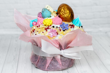 Easter cake with golden and colorful eggs on the top, sophisticatedly decorated, candies, sugar flowers, icing, meringue, and pink ribbon on white background. Copy space.