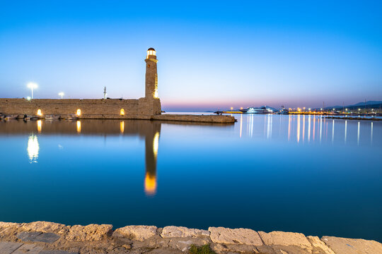 Old lighthouse reflected in the calm sea during the blue hour, Rethymno, Crete island, Greek Islands