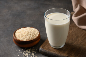 Sesame milk and with sesame seeds in wooden bowl on brown background. Close up. Vegan healthy milk...