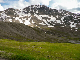 Panoramic view of the beautiful landscape in the Alps with fresh green meadows and blooming flowers and snow-capped mountain tops in the background on a sunny day with blue sky and clouds in spring