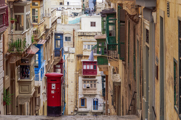 Typical street scene of alley with traditional homes, colorful balconies and red post box, Valletta, Malta
