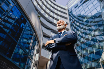 Low angle view of a proud senior businessman standing at the business center. - obrazy, fototapety, plakaty