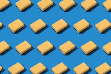 Pattern with yellow dishcloth on blue background. Household products and cleaning concept, selective focus