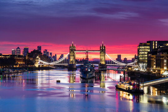 Tower Bridge and HMS Belfast reflecting in a still River Thames at sunset, London