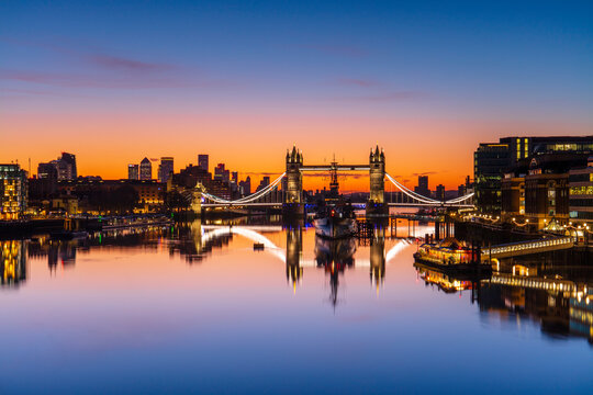 Tower Bridge, HMS Belfast and reflections in a still River Thames at sunrise, London