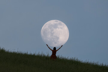 Full moon portrait at blue hour with a girl holding the moon above her head, Emilia Romagna