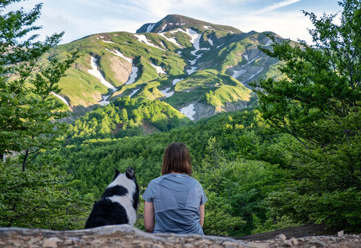 A girl sitting beside her border collie dog staring at a mountain landscape of Cusna Mountain, Emilia Romagna
