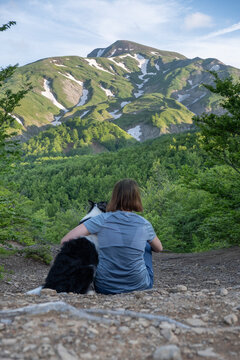 A girl sitting beside and hugging her border collie dog staring at a mountain landscape of Cusna Mountain, Emilia Romagna