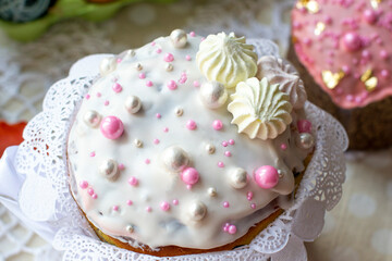 Top of a cake covered with white icing and decorated with pink and pearl balls and meringues