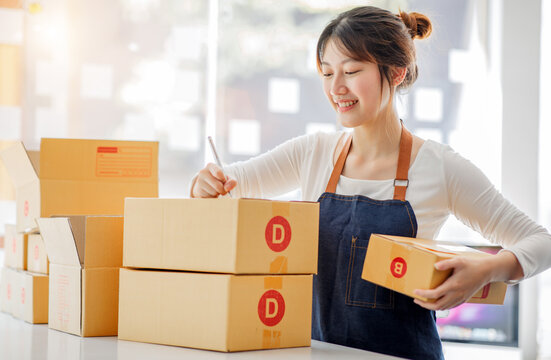 Startup happy Asian woman business owner works with a box at home, prepare parcel delivery SME supply chain, procurement, package box to deliver to customers, Online SME business entrepreneurs ideas,
