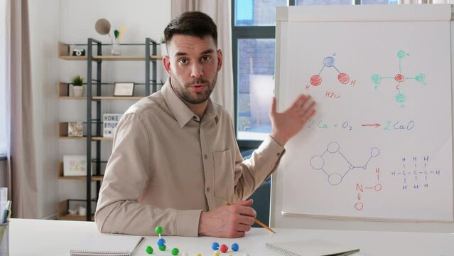 distance education, school and video blogging concept - male chemistry teacher with flip chart showing molecular formula having online class at home office