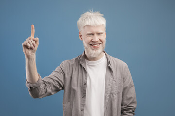 Handsome young albino guy pointing upwards experiencing AHA moment, having creative idea, gesturing eureka - obrazy, fototapety, plakaty