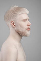Profile portrait of young bearded albino man with naked shoulders, posing over grey studio background