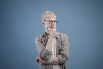 Let me think concept. Pensive unusual albino guy thinking and touching chin, blue studio background