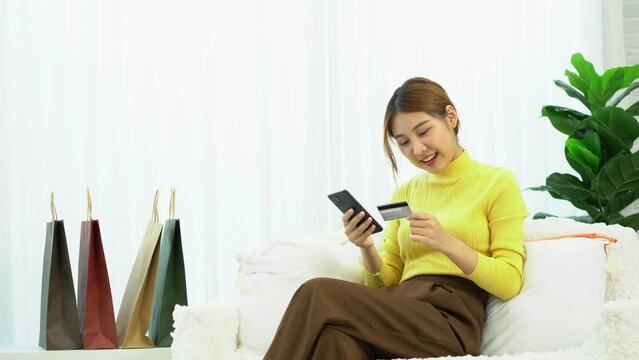 Asian women hold credit cards using digital mobile devices and shop online, type bank card numbers on smartphones, and transact using mobile banking applications. online shopping concept