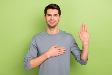 Photo of cute young brunet guy pray wear grey shirt isolated on green color background