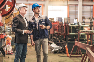  Factory owner, in a suit, stands and talks to the male foreman in charge of the machinery inspecting the steel production line in the steel plant.