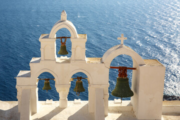 View on calm sea surface through traditional Greek white church arch with cross and bells in...