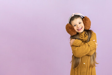 A teenager in warm headphones hugged himself smiling, a little girl in an autumn sweater on an isolated background, warm clothes in the cold season.