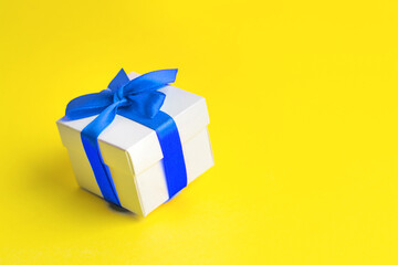 White box with a blue ribbon on a yellow background, copy space. Ukrainian gift concept. Copy space