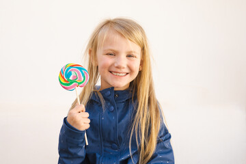 Happy smiling child with sweet lollipop having fun over white background outdoors