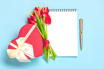 Obraz premium Bouquet of red tulips, gift box heart, notepad on blue background Top view Flat lay Holiday greeting card Happy moter's day, 8 March, Valentine's day, Easter concept Copy space Mock up
