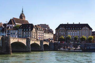 Fototapeta premium View of the old town of Basel, Switzerland, with an ancient stone bridge over the Rhine river and historical buildings and a church with a high sharp spire, a tourist ship at the pier