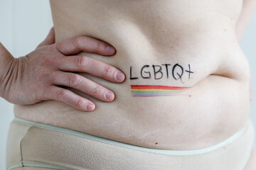 Woman with hand on waist and belly painted with rainbow flag LGBTQ+