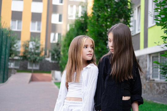 fraternal twins sisters. blonde and brunette teen girls in fashionable black and white clothes outdoors. sisterhood, siblings spending time together.