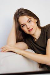 Fototapeta premium Happy young woman sitting on sofa at home and looking at camera. Portrait of comfortable woman in winter clothes relaxing on armchair.