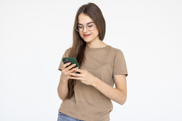 Pleased brunette woman in t-shirt writing message on smartphone isolated over white background