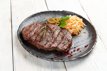 Cooked ribeye steak in a plate. On a light background.