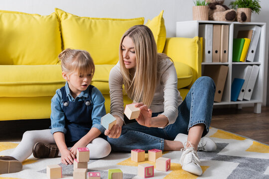 Speech therapist holding wooden blocks near child in consulting room.