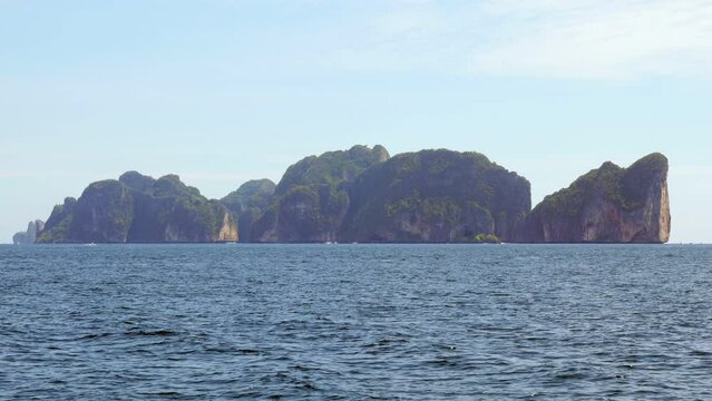 Rocky island, Koh Phi Phi Le, seen from fast moving boat, telephoto view. Ripply sea water on foreground, steep rocks of famous island seen from ferry boat sailing to PhiPhi Don
