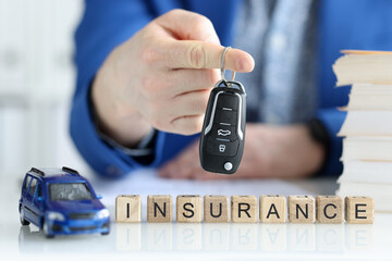 Agent holding car keys near wooden cubes with word insurance closeup
