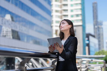 smart caucasian working woman in black suit standing, working with tablet and looking at copy space outside building in city