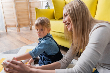 Smiling speech therapist holding wooden block near child in consulting room.